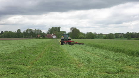 tractor mowing grass in green agricultural field under dramatic sky, slow motion wide view