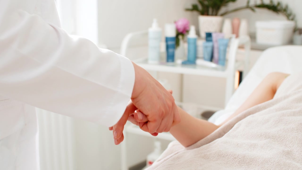Kosmetolog giver afslappende håndmassage til kvindelig klient under skønhedsbehandling i kliniksalon