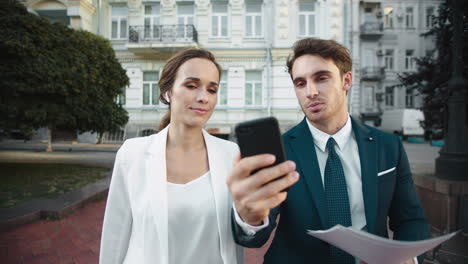 Friendly-business-man-showing-smiling-woman-information-on-phone