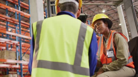 Diverse-male-and-female-workers-wearing-safety-suits-and-talking-in-warehouse