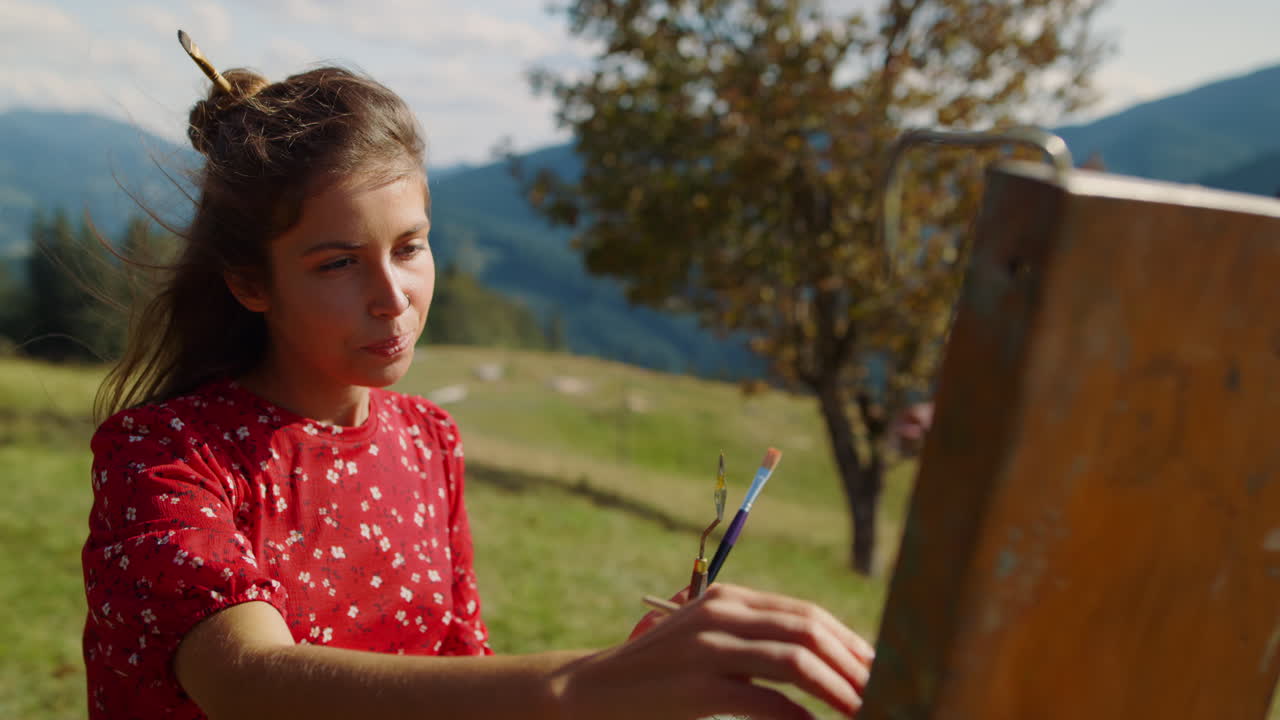 Closeup woman painter drawing picture in mountains. Girl painting on easel.