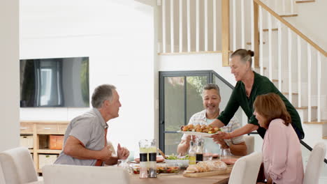 Serving food, woman enjoying meal with senior friends at dining table, copy space