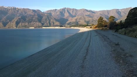 wide smooth aerial along the beach at the south of lake hawea on new zelands south island, a popular swimming spot with locals and tourists alike