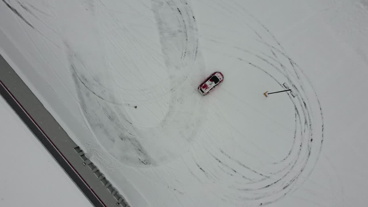 Experience the thrill of a drone's eye view as it captures a red car racing through a snowy parking lot on a winter day