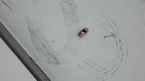 experimente la emoción de la vista de un dron mientras captura un auto rojo corriendo a través de un estacionamiento nevado en un día de invierno