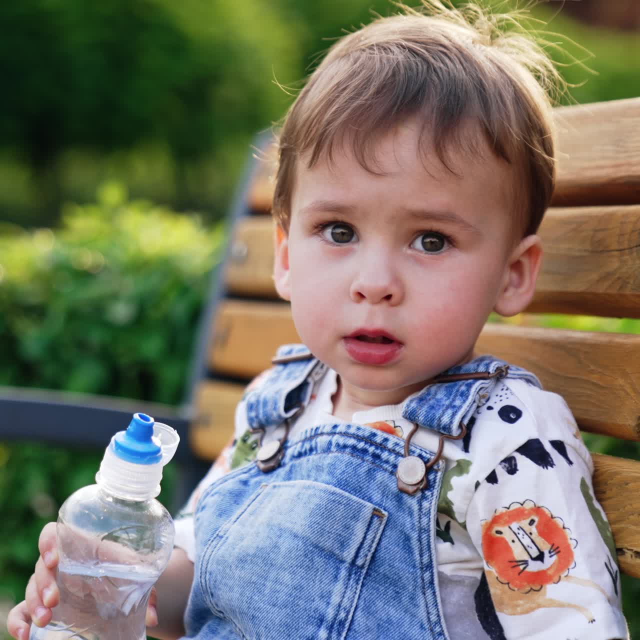 Lovely baby boy sitting on the bench. Portrait of a toddler talking to camera