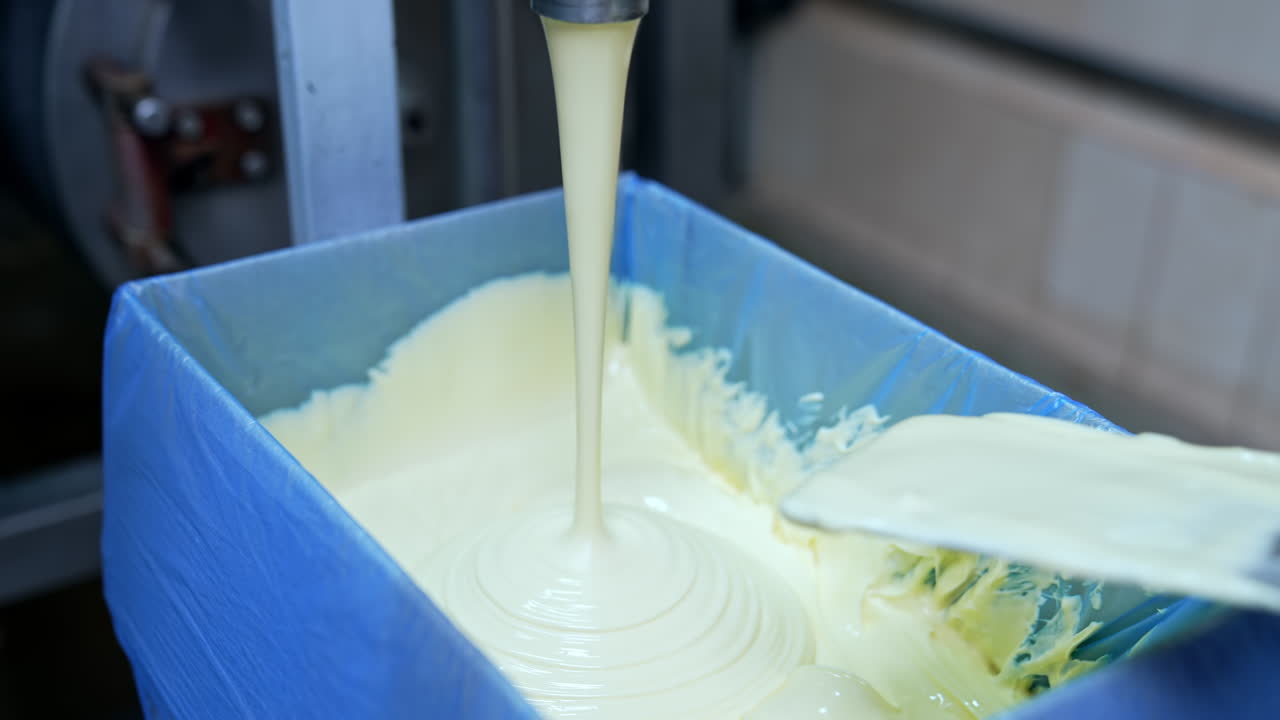 Factory for butter production. Creamy white dairy product pouring into box. Making fresh butter on a milk farm. Dairy product manufacturer. Hand of worker is mixing butter. Close-up.