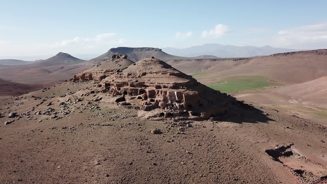 Stunning 4K wide aerial of an ancient rock-cut village on a desert hillside. Highlights historical cave dwellings and arid terrain. Perfect for cultural and historical documentaries