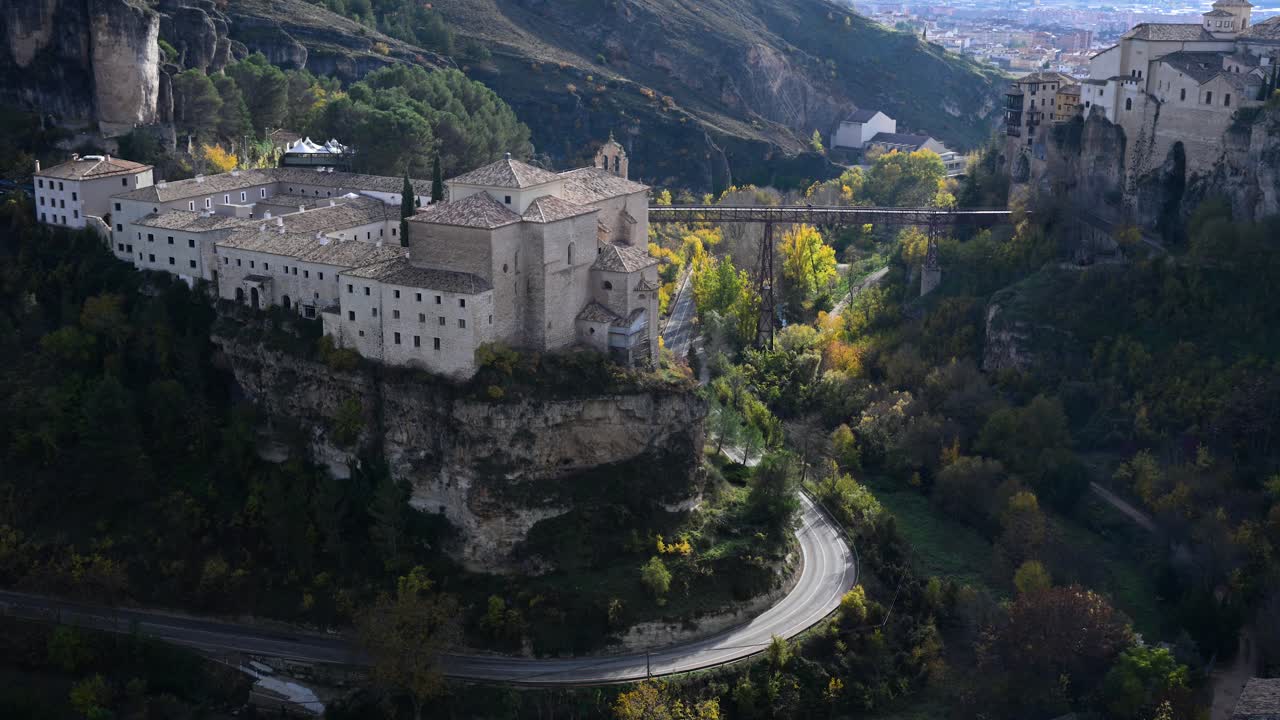 Vibrant autumn foliage colors the landscape around the historic city of Cuenca, Spain, framing the Parador hotel and the iconic Hanging Houses on the cliffs.