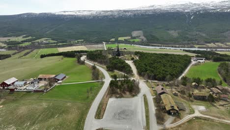 Lesja-Church-laying-on-top-of-a-small-hill-at-Innlandet-Norway---Aerial-approaching-church-above-the-road