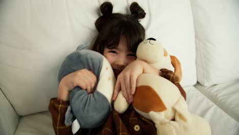 little shy girl embrace her soft toys while sit on the sofa