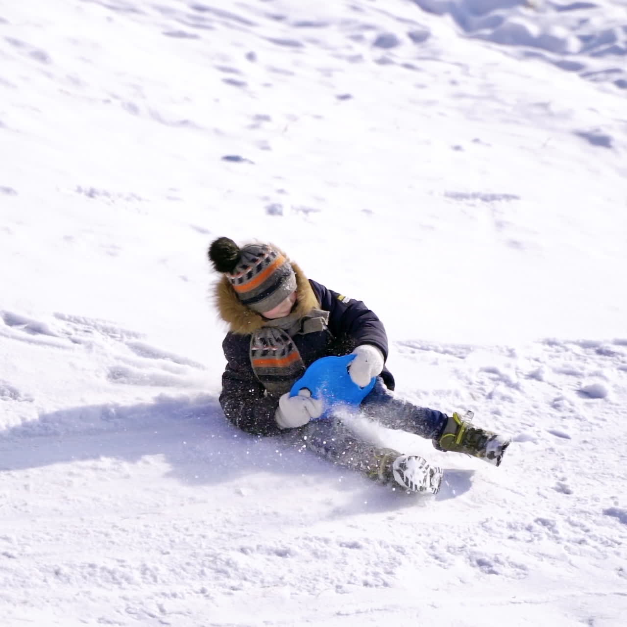 Boy sledging down the hill. Ice slide at winter park. Happy kid riding on a plastic plate on snow.