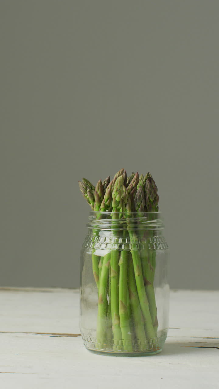 회색 배경 에 있는 유리 항아리 에 있는 신선 한 아스파라거스 줄기 의 수직 비디오