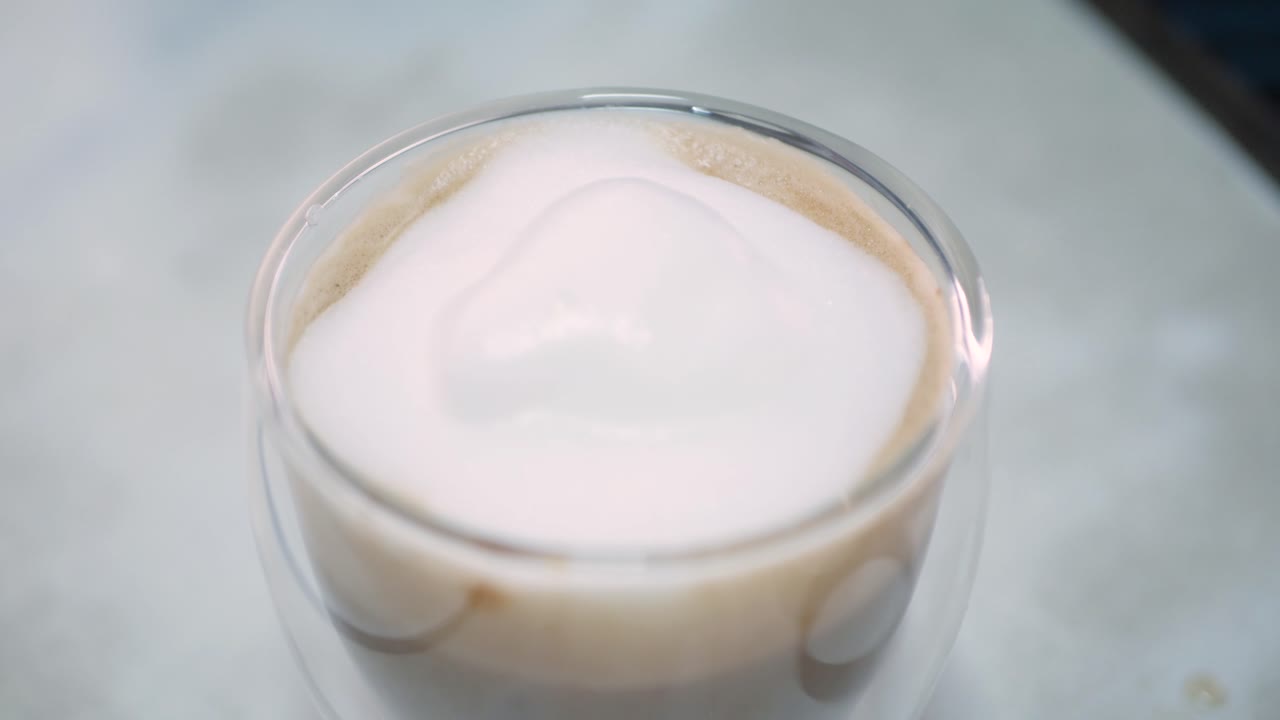 Putting a hot frothing milk bubble into a cup of fresh cappuccino coffee for breakfast drink