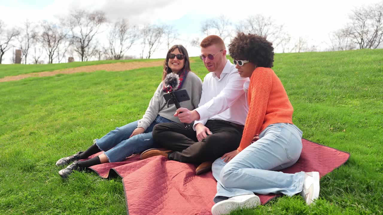 Amigos grabando un vlog en una manta de picnic en el parque
