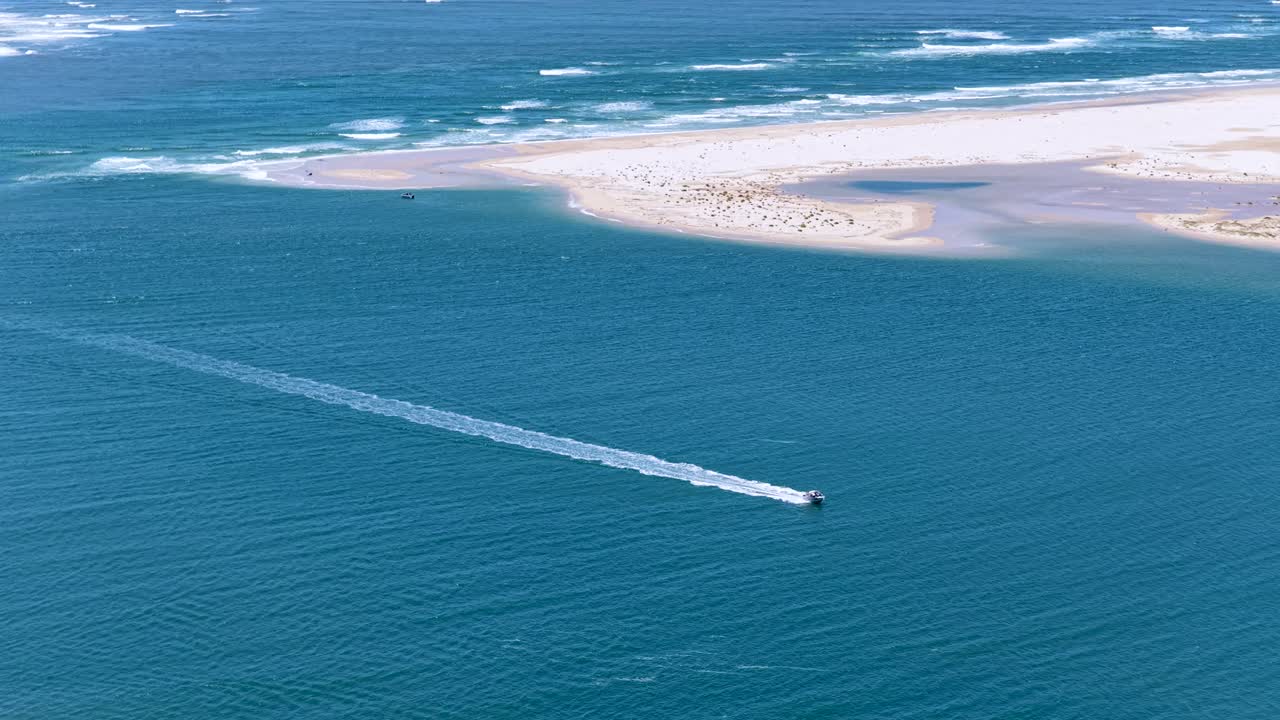 Immagine aerea ad angolazione elevata di un motoscafo che naviga nelle acque costiere blu vicino a un banco di sabbia