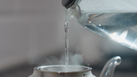 close up of pouring hot water into glass kettle with steam rising, focusing on water flow and steam emanating from the kettle, ideal for kitchen, beverage, tea making, and culinary content