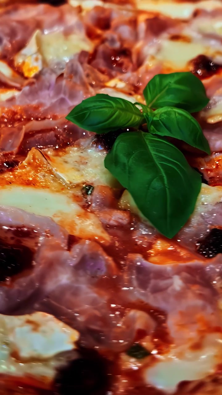 Pizza appena sfornata guarnita con foglie di basilico, vista in primo piano.