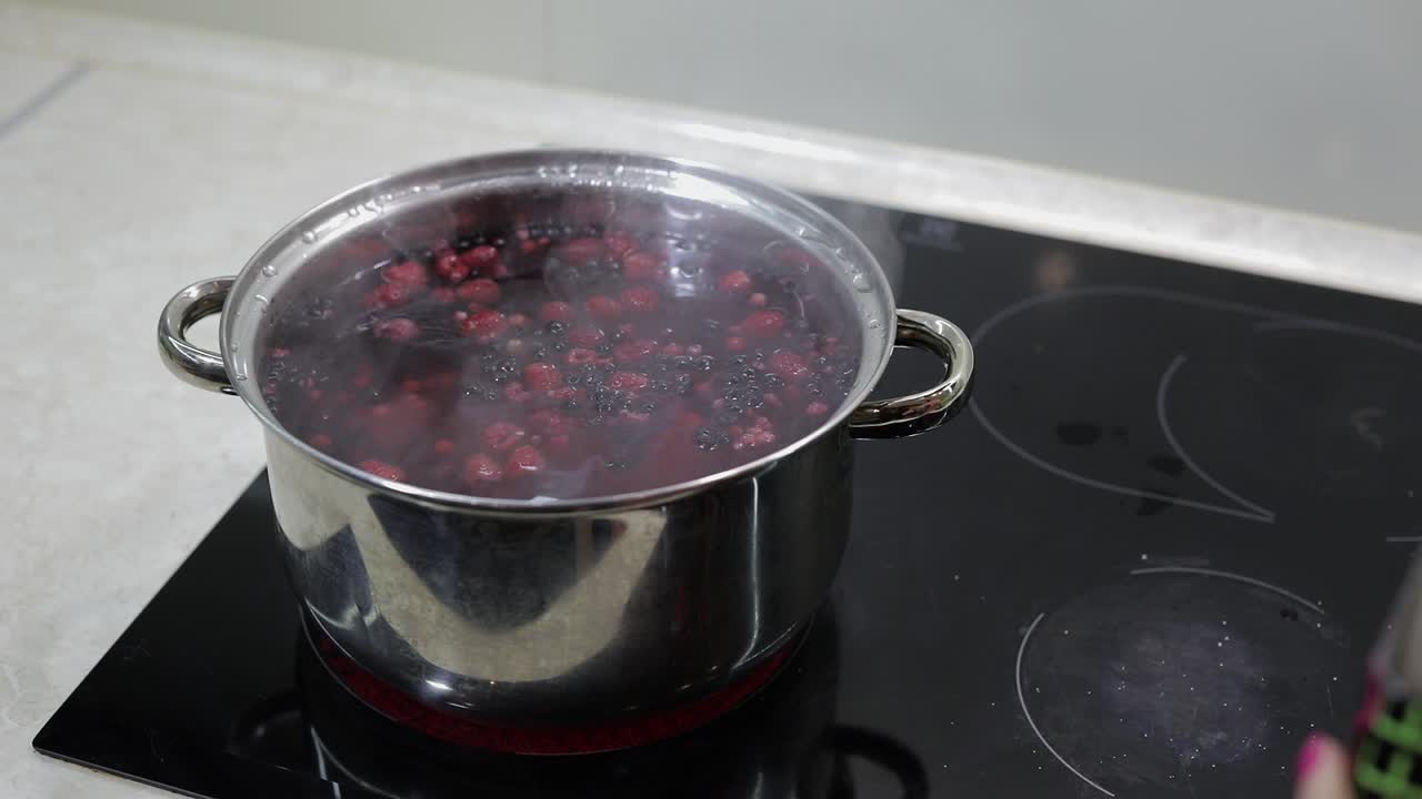 Bacche in pentola con acqua bollente. Aggiunta di zucchero. Preparazione della composta. Cucina.
