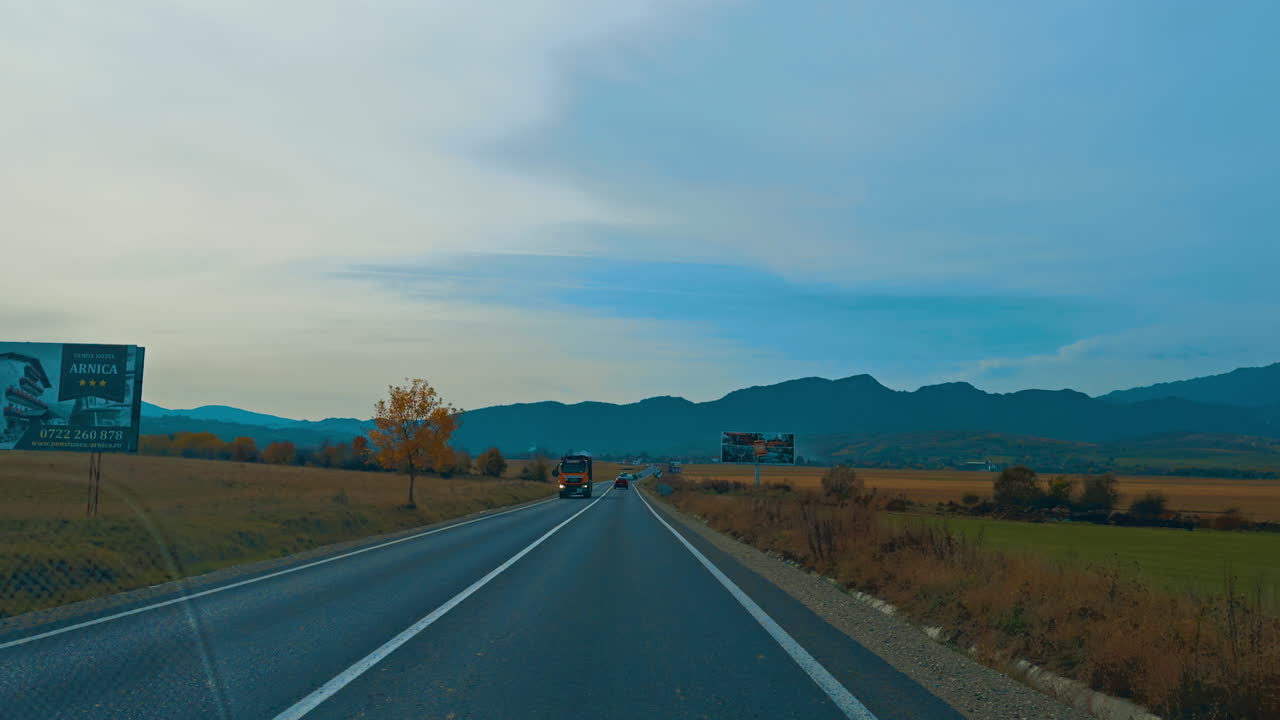 Riding by the good highway with a few cars on. Driving by the road leading to a mountain range.