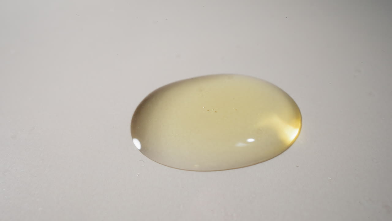 gotas pesadas de aceite de jojoba caen sobre la mesa reflejando la luz