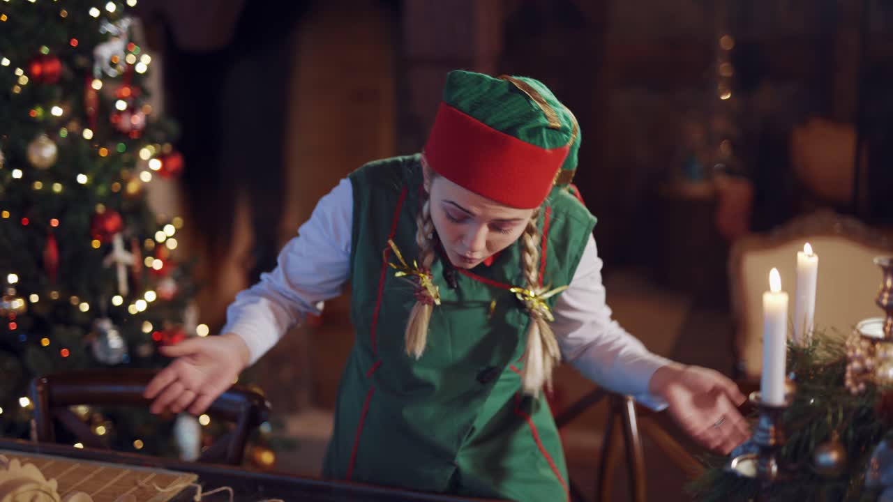 Funny elf holding stack of envelopes for Santa. Dispersed young elf with letters. Envelopes falling on the table from girl's hands on the Christmas tree background.