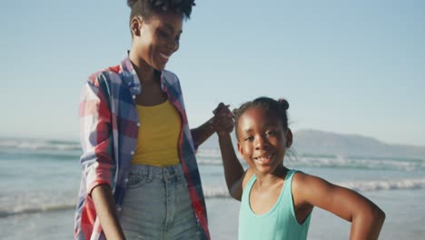 madre afroamericana sosteniendo la mano de su hija y caminando por la playa