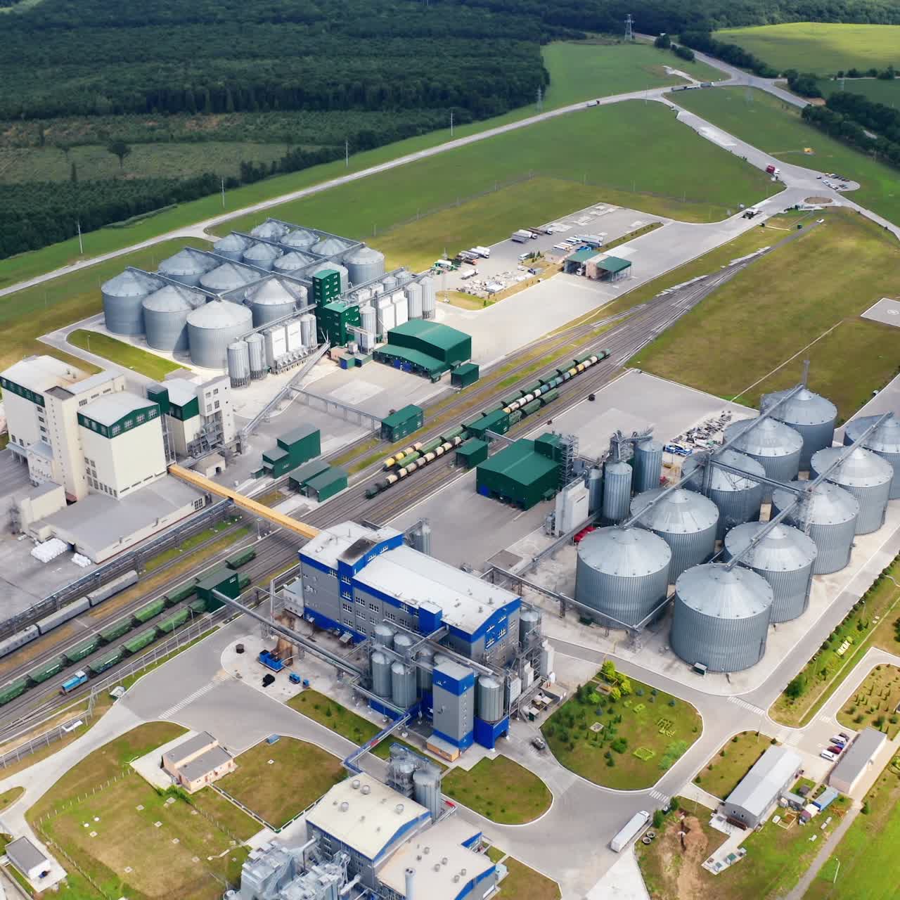 Large granary in field. A new built-in industrial grain elevator among nature. Silver containers for storing agricultural products. Aerial view