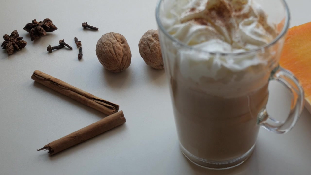 Panoramica su una tazza di vetro trasparente con caffè o cacao con panna, cannella, zucca e chiodi di garofano. Sapori natalizi.