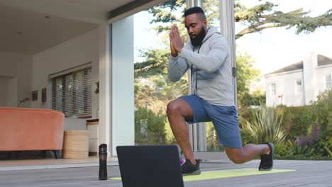 Hombre-Afroamericano-Enfocado-En-Entrenamiento-Físico-Estirándose-En-Cubierta-En-Un-Jardín-Soleado,-Cámara-Lenta