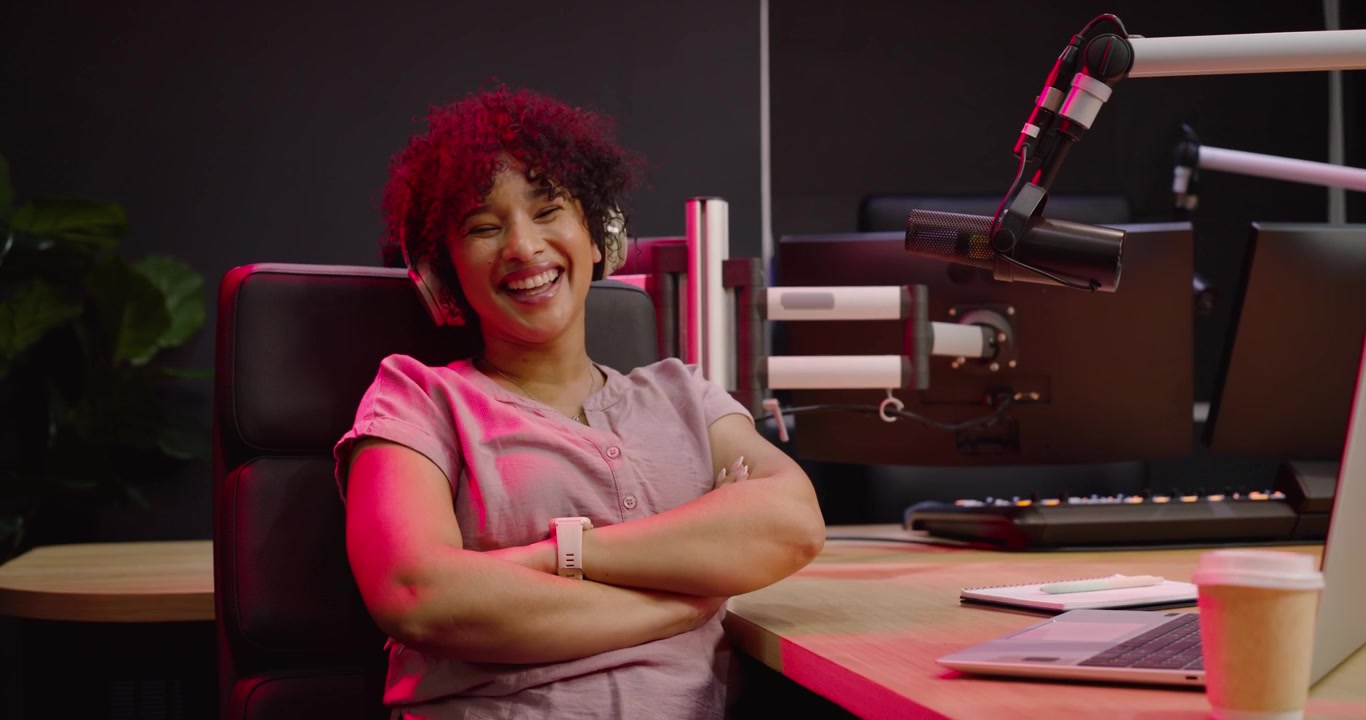 Donna afroamericana con cuffie che digita sul laptop in studio, regola il microfono e si prepara a registrare.