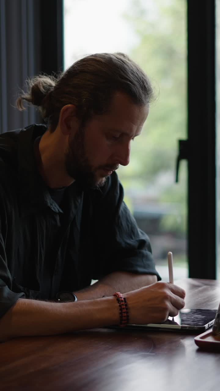 A man drawing on a tablet near a window