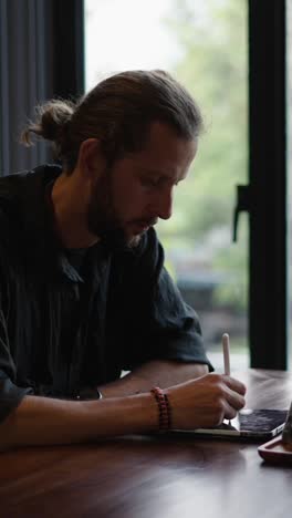a man drawing on a tablet near a window