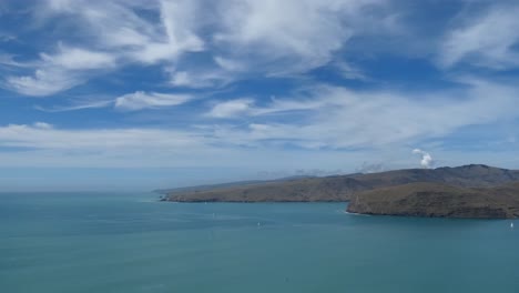 Wispy-cirrus-clouds-contrast-with-extinct-volcano-and-turquoise-ocean---Banks-Peninsula,-New-Zealand