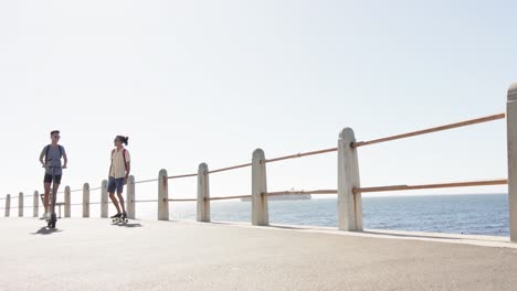 Happy-diverse-gay-male-couple-using-scooters-at-promenade-by-the-sea,-slow-motion