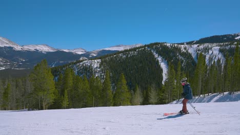 slow motion of one skier on a bright sunny day with other ski slopes in the distance along the rocky mountains