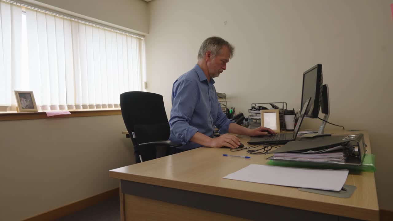 Sitting businessman in an office typing on his laptop, locked off