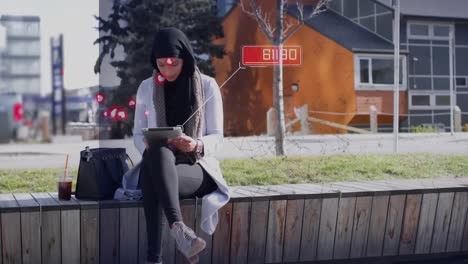 red de conexiones y múltiples iconos digitales flotando sobre una mujer en hijab usando una tableta digital
