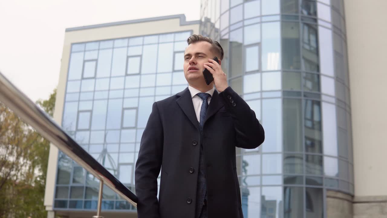 Young elegant businessman talking on phone near the office center