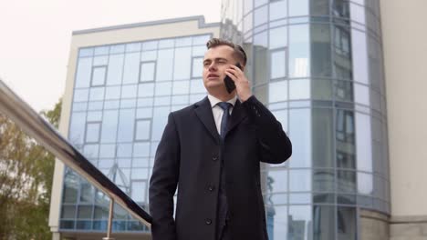 young elegant businessman talking on phone near the office center