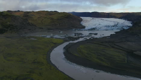 Aerial-drone-cinematic-upward-reveal-pan-motion-of-Solheimajokull-glacier-Iceland-lagoon,-river,-streams-and-icebergs-late-afternoon