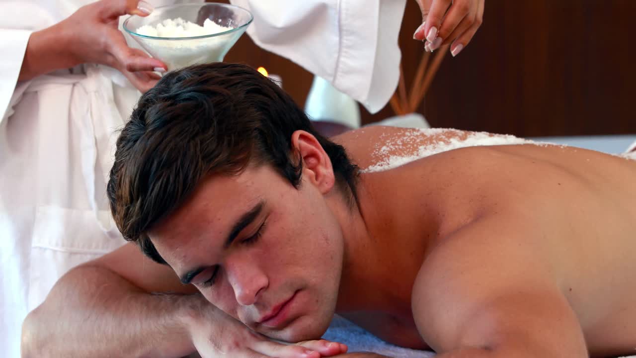 예쁜 남자가 소금 스크러브 치료를 받고 있습니다.