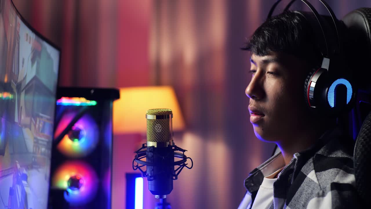 개인 컴퓨터에서 네트워크를 통해 게임을하는 동안 허리 통증이있는 아시아 소년 스트리머의 가까운 측면 뷰 라이브 스트리밍 비디오 게임, rgb led 스트립 라이트에 의해 조명 된 책상