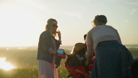 two sisters are diligently cleaning a red power bike in a serene, open grassy field, one focuses on wiping the bike s glass while the other carefully cleans the tank under the golden sunlight