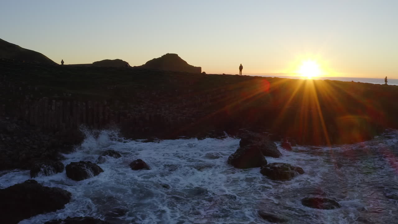 Aerial pan gliding near Giant's Causeway shore at sunset with vibrant sun flares