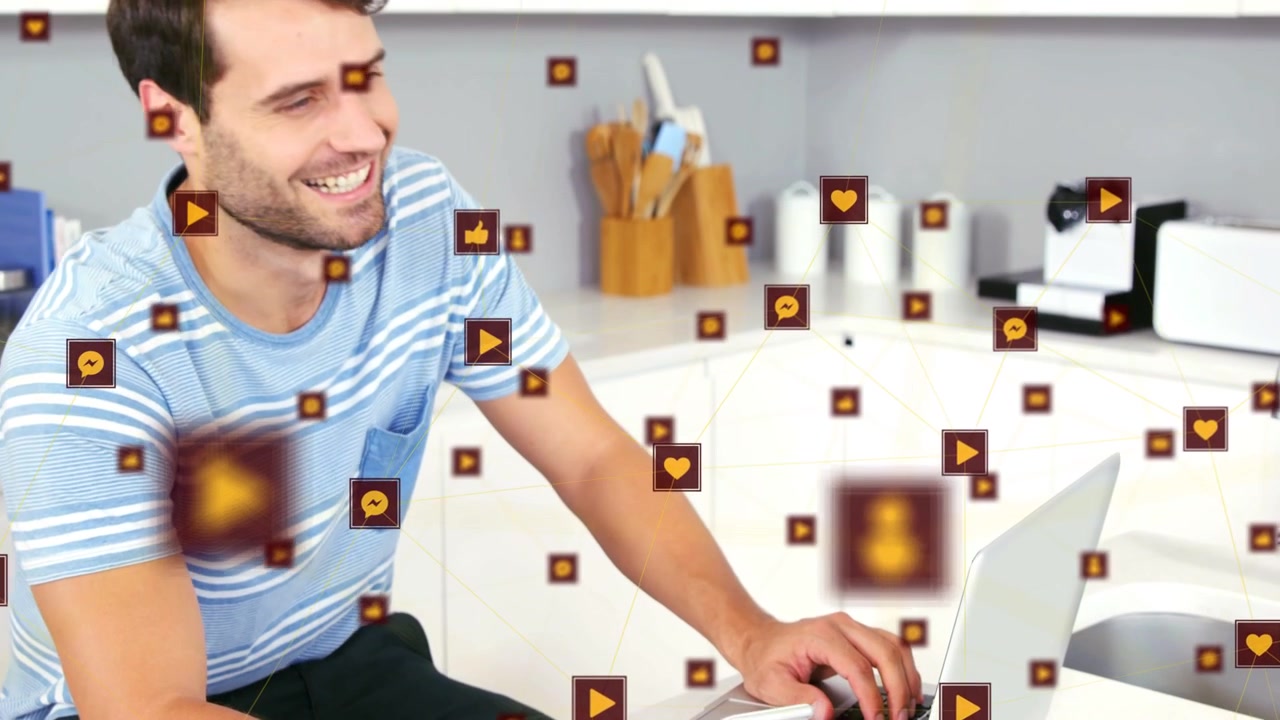 Uomo adulto che digita sul laptop e tocca il telefono in cucina, creando icone animate e gestendo contenuti.