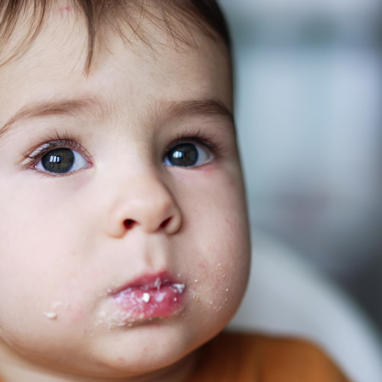 Beautiful little kid eating dairy from spoon. Adorable child takes a spoonful into mouth and then looks up thoughtfully. Close up