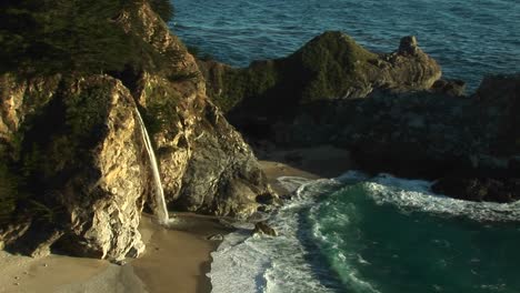 birdseye shot of a waterfall crashing down into a secluded pool of the california pacific ocean