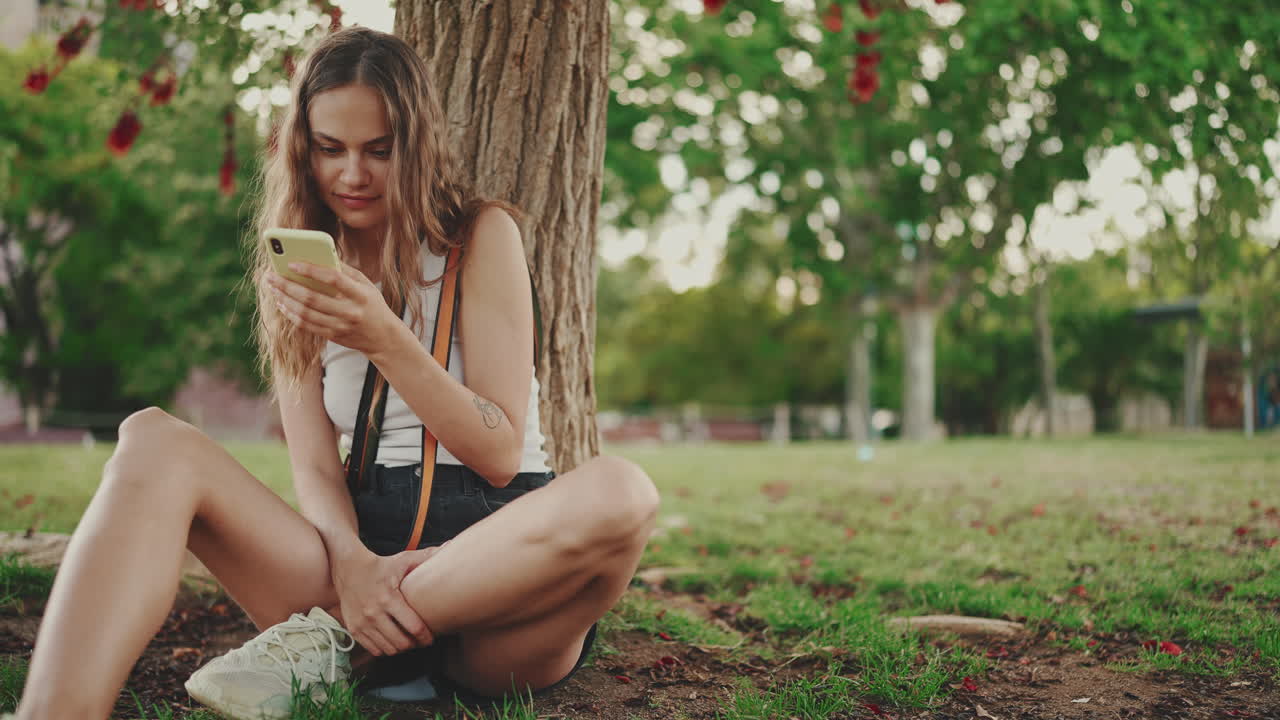 Woman with phone sitting by a tree in a park