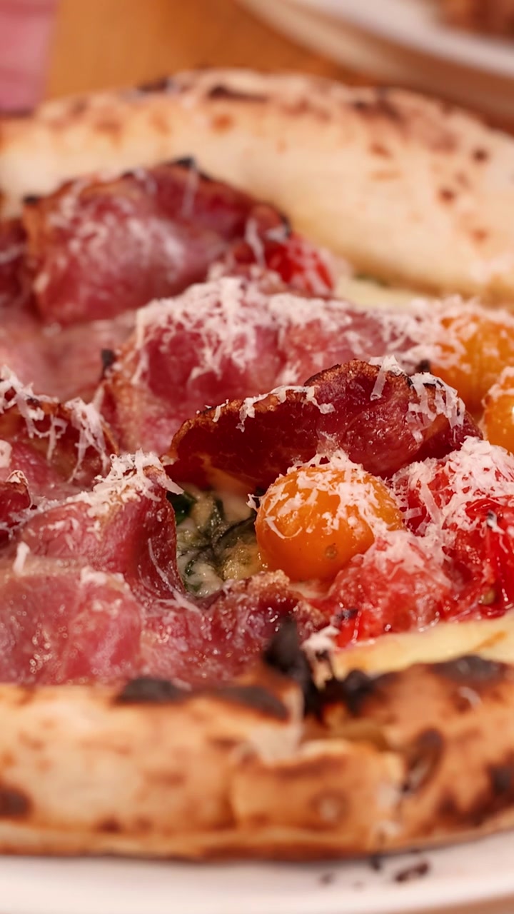 Primo piano di pizza appena sfornata con prosciutto e pomodorini.
